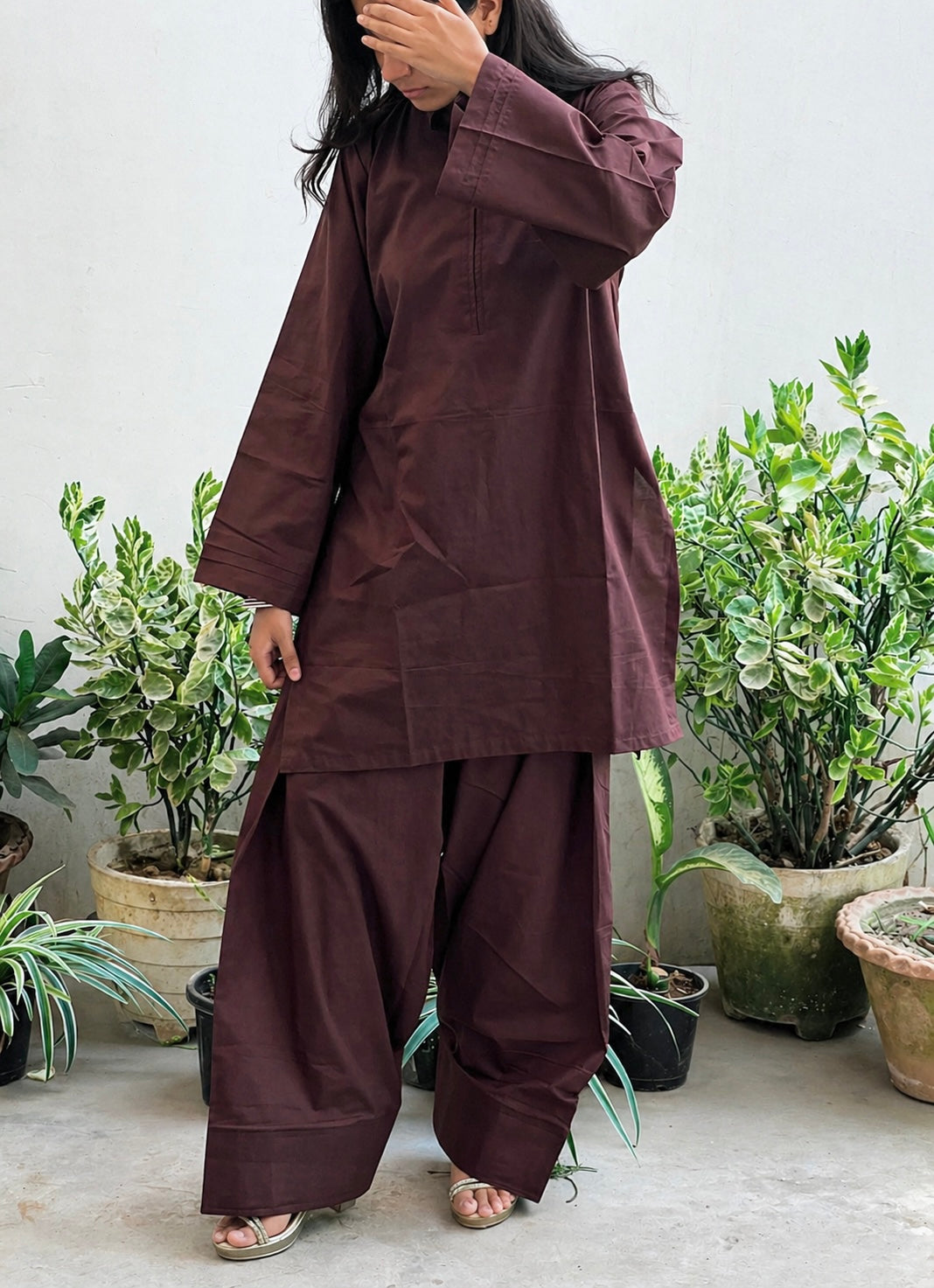Person wearing a brown traditional outfit standing among potted plants.
