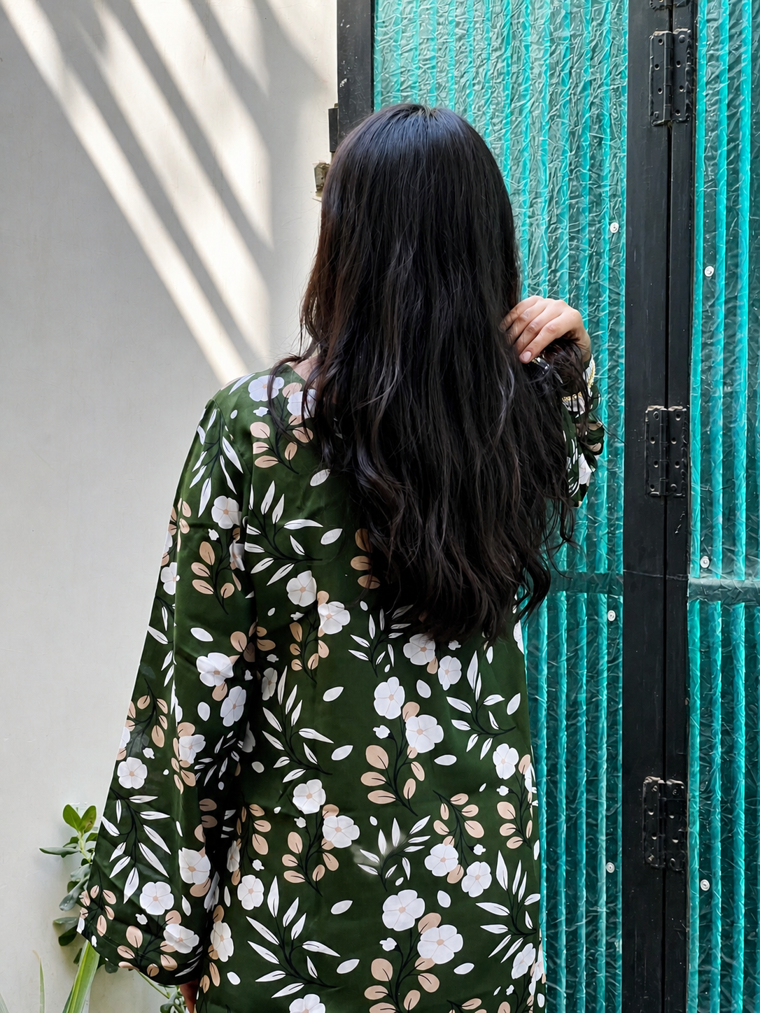 Person wearing a floral dress standing in front of a textured green wall.
