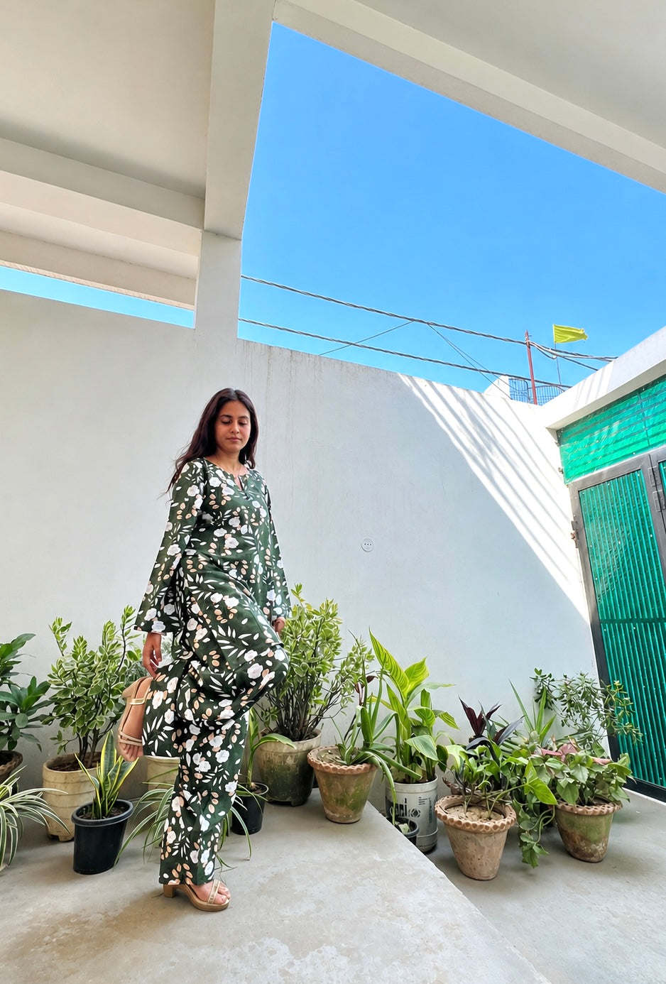Woman standing in a modern outdoor area with plants and a clear blue sky.